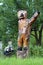 Vintage retro bear waving hello wooden sculpture next to small turtle sculpture on two cut down tree stumps surrounded with grass