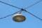 Vintage retro old style large round street lamp within metal casing suspended with dark electrical wires above street crossroads