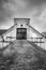 Vintage rural scene, dramatic front view of black and white old rustic worn stone barn farmhouse building with dark sky. Arched st