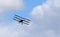 Vintage Sopwith Triplane in flight with clouds and blue sky.