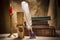 Vintage still life with glasses on old books near inkstand, feather, old paper and burning candle on canvas background