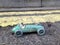 Vintage toy racing car & driver close up with worn green patina, in front of double yellow line no parking restriction.