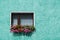 Vintage traditional glass window decorated with hanging pink and red petunias in the blue green facade of a house