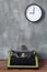 Vintage typewriter at wooden table near wall with clock