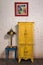Vintage yellow cupboard, painting, brass table lamp and vintage table on dark wooden parquet floor and white bricks wall