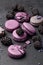 Violet and lilac macarons and blackberries on black concrete background