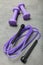 Violet rope and dumbbells for fitness on a concrete background
