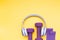 violet rubber expanders, purple dumbbells and headphones worn on them on a yellow background, copy space, top view