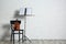 Violin, chair and note stand with music sheets near brick wall.