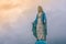 Virgin Mary statue at Catholic church with sunlight in cloudy day background.