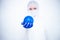 A virologist in a white mask and blue rubber gloves in a viral protective suit on a white background holds a blue ball in the form