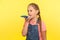 Virtual assistant. Portrait of little girl with braid in denim overalls talking to mobile phone using digital voice app