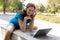 Virtual date. Smiling friendly caucasian woman in wireless headphones sits on a parapet and chatting on a laptop in the