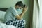 Virus outbreak - dramatic portrait of sick man in medical facial mask sitting on bed scared and worried infected by coronavirus