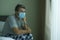 Virus outbreak - sick man wearing medical facial mask sitting on bed scared and worried infected by coronavirus suffering lockdown