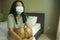 Virus outbreak - young beautiful desperate and worried Asian woman wearing medical face mask in quarantine and lockdown at home in