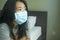 Virus outbreak - young beautiful desperate and worried Asian woman wearing medical face mask in quarantine and lockdown at home in