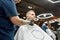 Visiting barbershop. Young handsome man sitting in armchair in barber salon while professional barber trimming beard