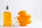Vitamin C serum in cosmetic bottle with dropper, sliced orange and flowers on white background. Organic SPA cosmetics with herbal