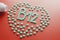 Vitamins B 12 in the shape of a heart on a red substrate, poured out of a white jar.