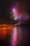 Vivid multicolour fireworks with red and purple sparks on dark sky with reflection in the lake. Fun and joyful holiday background