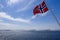 Vivid Norwegian flag billows against a summer sky, with snowy mountains