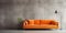 Vivid orange corner velvet sofa near concrete wall with copy space. Minimalist interior design of modern living room