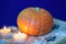 Vivid orange pumpkin on the open book, candles, stars and blue background
