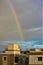 Vivid rainbow arches over a bustling cityscape of rooftops and tall buildings