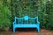 Vivid turquoise blue colored wooden bench on the terracotta brick pathway in green garden