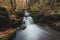 Vlasky River with waterfall illuminated with sun in an untouched landscape in the middle of an autumn mixed forest in red-orange