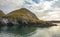 Volcanic Island off the fjords of western Iceland under cloudy blue sky with calm green water in foreground