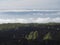 Volcanic landscape with lava fields partly covered by the pine tree forest above clouds with silhoutte of La gomera