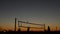 Volleyball net silhouette on beach court at sunset, players on California coast.