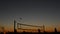 Volleyball net silhouette on beach court at sunset, players on California coast.