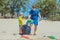 Volunteer blue face mask forest sand beach. Son helps father hold black bag for pick up garbage. Problem spilled rubbish