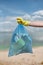 Volunteer or eco activist wearing yellow rubber gloves holding trash bag with plastic waste and other garbage against