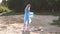 A volunteer girl in gloves collects garbage on the beach in a garbage bag.