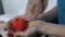 Volunteer holding toy heart in palms, sick female patient sleeping on background