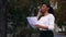 Volunteer talking on phone with sponsor for charity concert, smiling lady standing on street near trees