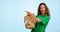 Volunteer woman, point and donation in studio, smile and face with vegetables for charity by blue background. Girl, bag