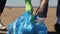 Volunteers in gloves go to bag and put collected trash plastic in Spbi. closeup of bag on beach sand