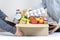 Volunteers hands holding food donations box with grocery products on white desk