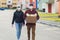 Volunteers in protective masks walk down the street with a box of groceries, charity