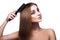 Voluptuous girl with blue eyes combing her perfect healthy streight brown hair with comb on white background