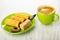 Wafer rolls, spoon, sugar in saucer, green cup with coffee on wooden table