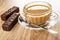 Wafers in chocolate, cup of coffee with milk, spoon on saucer on wooden table