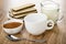 Wafers with porous chocolate in plate, pitcher with milk, cocoa with sugar in bowl, empty cup, spoon on wooden table