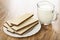 Wafers with porous chocolate in plate, transparent pitcher with milk on wooden table