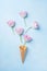 Waffle cone with flying pink tulips on pastel blue background top view. Flat lay style.